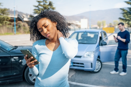 female rubbing her neck after a car accident while looking at her phone