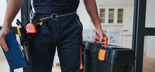handyman wearing a toolbelt and carrying a toolbox and clipboard